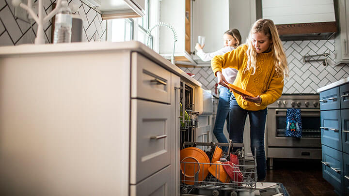 Two young girls helping put away dishes from a dish washer into a cabinet