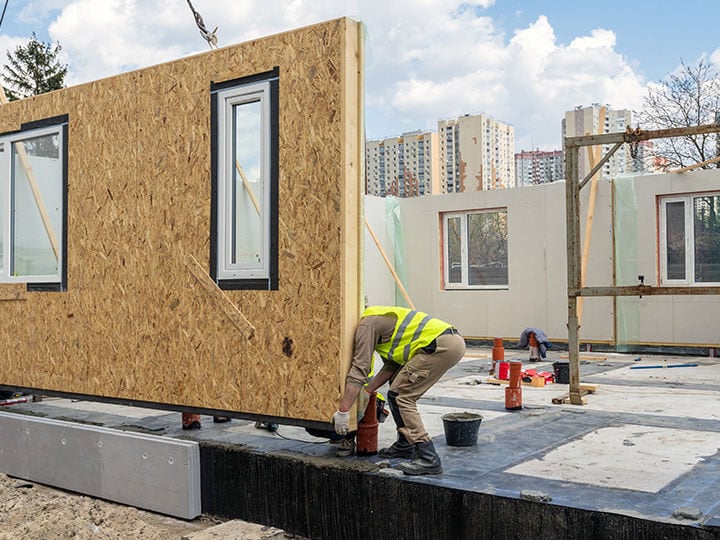 Construction worker in yellow caution vest, guiding a composite sip panel in place while constructing a new and modern modular house