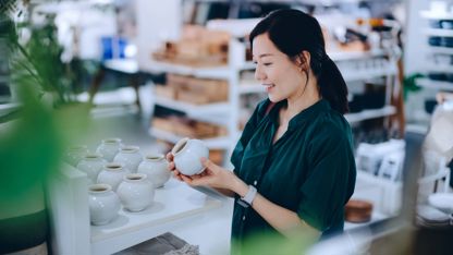 A woman stands in a store, holding a cup and examining its design with a thoughtful expression.