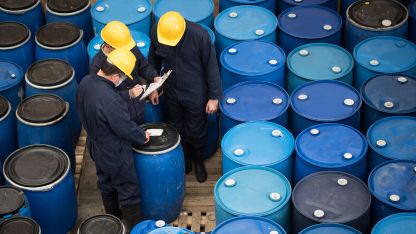 Two men in hard hats inspecting barrels at a construction site, demonstrating safety and teamwork in their work environment.